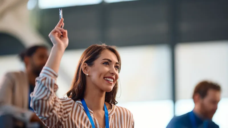 Asistente con credencial levanta la mano para preguntar durante un evento
